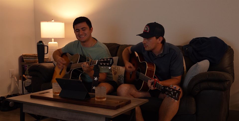 Caleb Borden and Matt Navarro playing acoustic guitars together in a lamp-lit living room